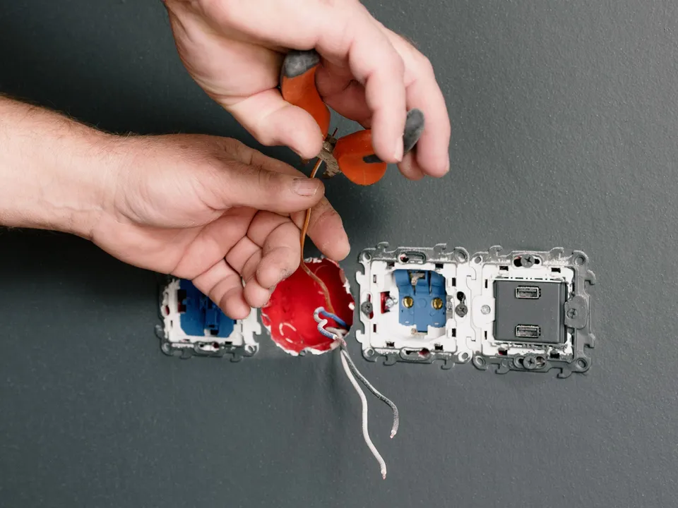 An electrician wiring a wall socket with pliers